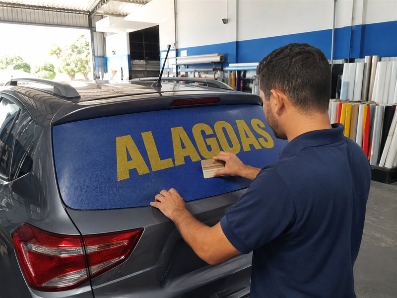 Aplicador instalando adesivo perfurado no vidro traseiro de um carro