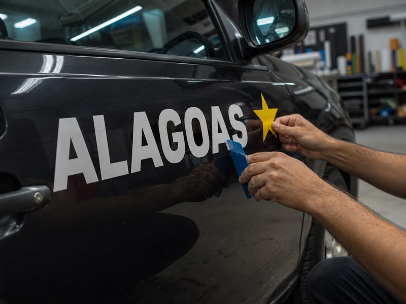 Aplicação de adesivo recortado em vinil na porta de um carro, com espátula